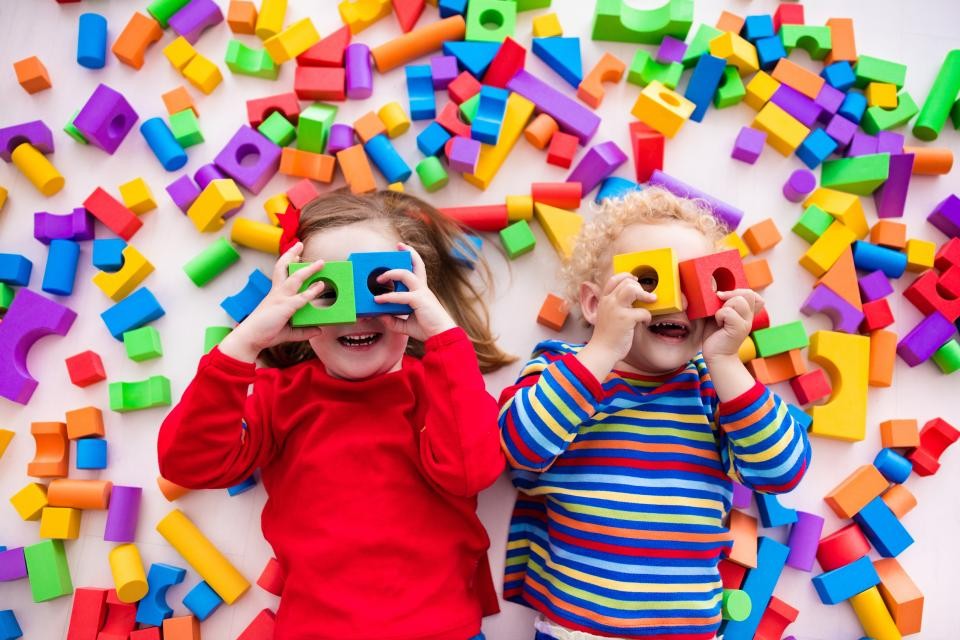 Zwei Kinder liegen auf dem Boden. Um sie herum liegen zahlreiche bunte Bauklötze.